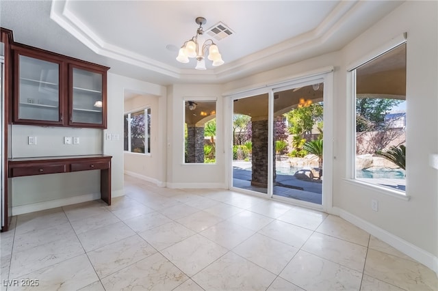 unfurnished dining area with a chandelier, a raised ceiling, and baseboards