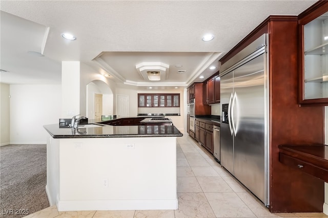 kitchen with appliances with stainless steel finishes, dark countertops, a raised ceiling, dark brown cabinets, and recessed lighting