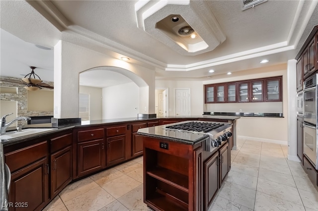 kitchen featuring a tray ceiling, a sink, appliances with stainless steel finishes, dark brown cabinets, and a kitchen island