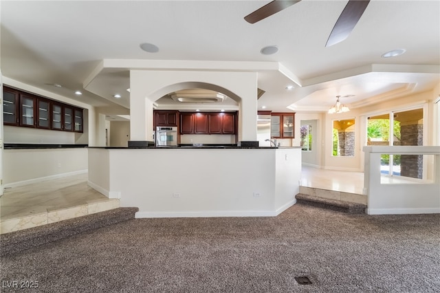 kitchen featuring oven, a tray ceiling, dark countertops, light carpet, and ornamental molding