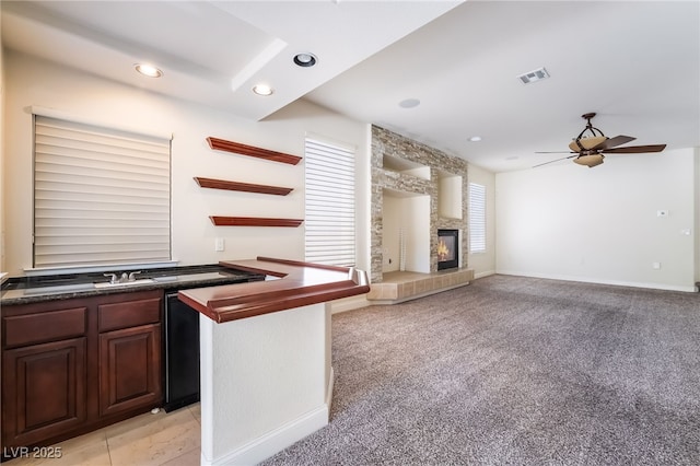 kitchen featuring dark countertops, a ceiling fan, a fireplace, recessed lighting, and light colored carpet
