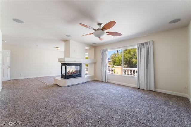 unfurnished living room featuring carpet, ceiling fan, a multi sided fireplace, and baseboards