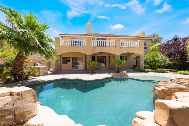 back of property with a balcony, an outdoor pool, exterior kitchen, and stucco siding