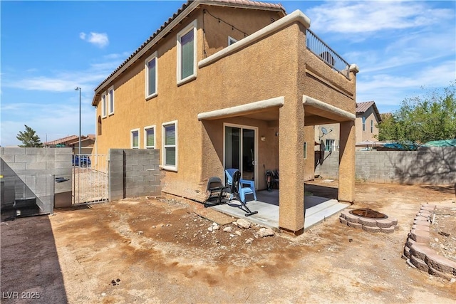 rear view of house with a fire pit, a gate, stucco siding, a patio area, and fence