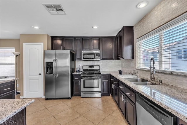kitchen with stainless steel appliances, a sink, decorative backsplash, light stone counters, and light tile patterned flooring