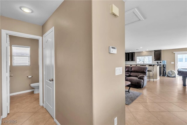 hall featuring light tile patterned floors, attic access, and baseboards