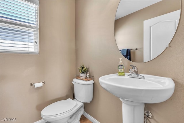 half bathroom with toilet, plenty of natural light, and baseboards