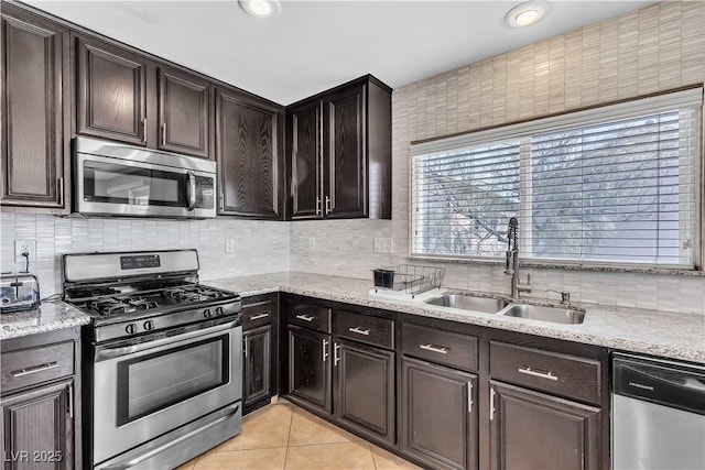 kitchen featuring appliances with stainless steel finishes, a sink, light tile patterned floors, decorative backsplash, and dark brown cabinets