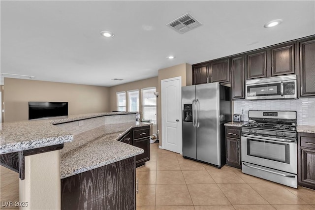 kitchen featuring stainless steel appliances, tasteful backsplash, light tile patterned floors, dark brown cabinets, and light stone countertops