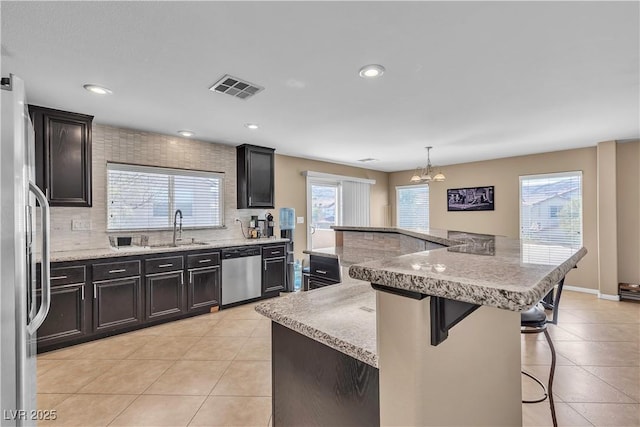 kitchen with appliances with stainless steel finishes, a sink, a kitchen bar, tasteful backsplash, and light tile patterned floors