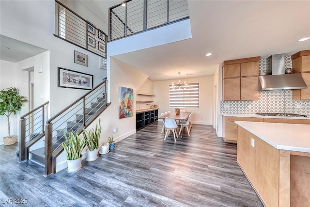 kitchen featuring wall chimney range hood, wood finished floors, stainless steel gas stovetop, a chandelier, and baseboards