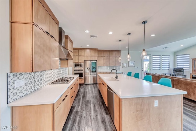 kitchen featuring appliances with stainless steel finishes, a sink, wood finished floors, decorative backsplash, and light countertops