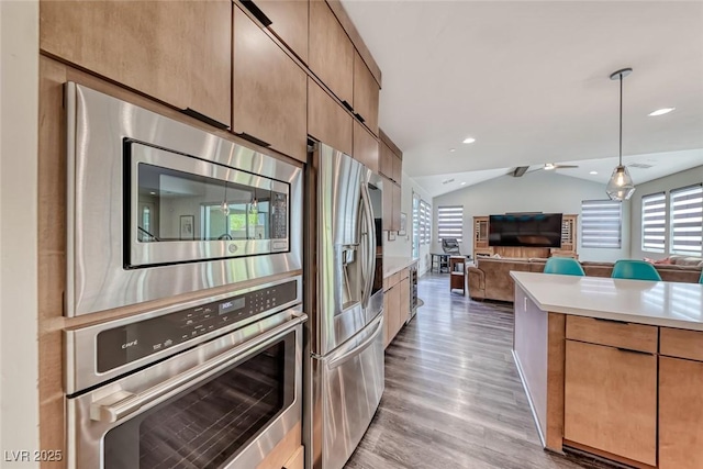 kitchen with appliances with stainless steel finishes, open floor plan, vaulted ceiling, light wood-style flooring, and light countertops