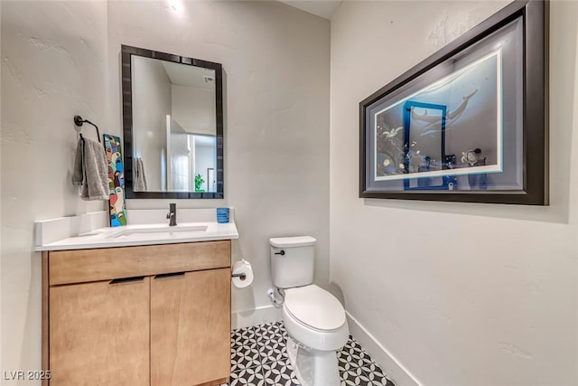 half bath with toilet, baseboards, vanity, and tile patterned floors