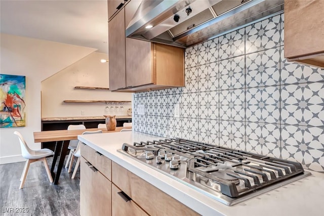 kitchen with stainless steel gas stovetop, wall chimney exhaust hood, light brown cabinetry, and decorative backsplash