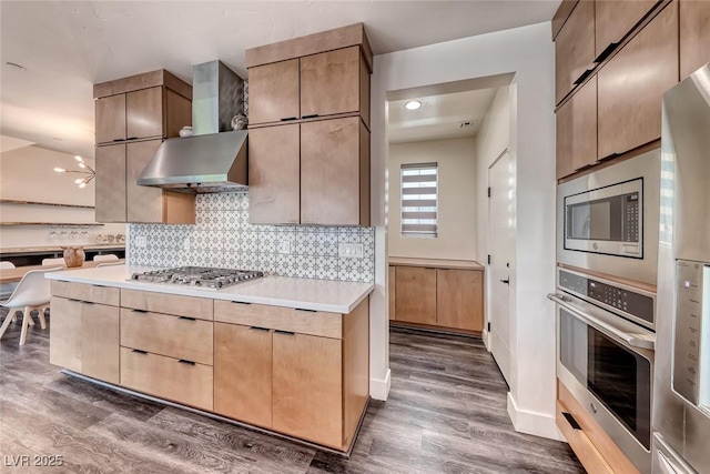 kitchen featuring appliances with stainless steel finishes, wall chimney range hood, dark wood-type flooring, and tasteful backsplash