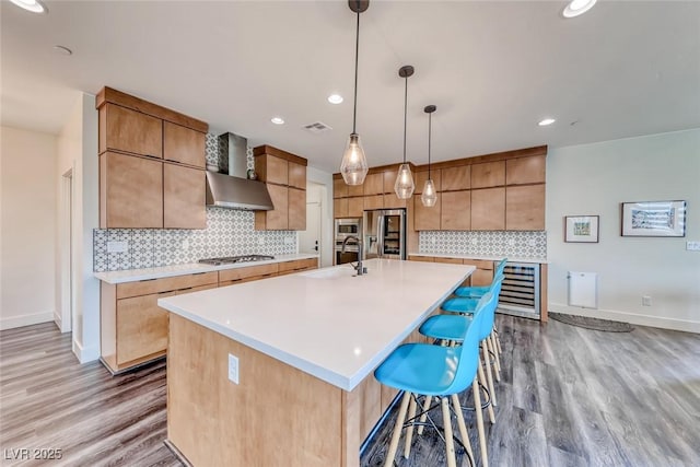 kitchen with a sink, wall chimney range hood, appliances with stainless steel finishes, light wood-style flooring, and recessed lighting