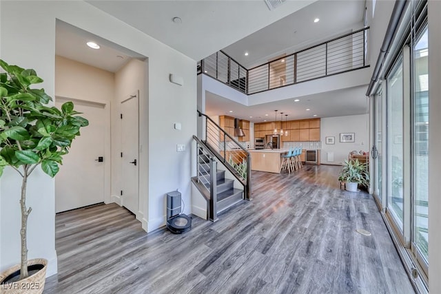 foyer with light wood-type flooring, stairs, baseboards, recessed lighting, and a high ceiling