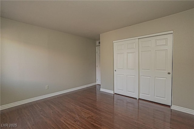 unfurnished bedroom featuring dark wood-style floors, baseboards, and a closet
