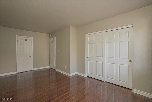 unfurnished bedroom with wood finished floors, baseboards, and a closet