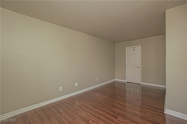 spare room with baseboards and dark wood-type flooring