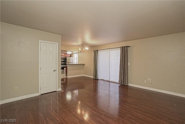 unfurnished living room featuring dark wood-type flooring, baseboards, and a chandelier
