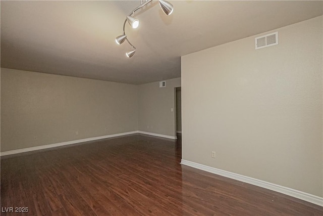 spare room featuring dark wood-type flooring, baseboards, and track lighting