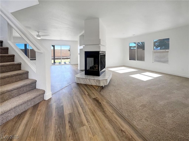983 Plantain Lily Ave, Las Vegas, NV 89183 - unfurnished living room featuring wood finished floors, stairs, a multi sided fireplace, baseboards, and a ceiling fan