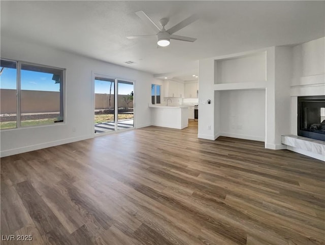 983 Plantain Lily Ave, Las Vegas, NV 89183 - unfurnished living room featuring ceiling fan, a fireplace with raised hearth, dark wood-type flooring, and baseboards