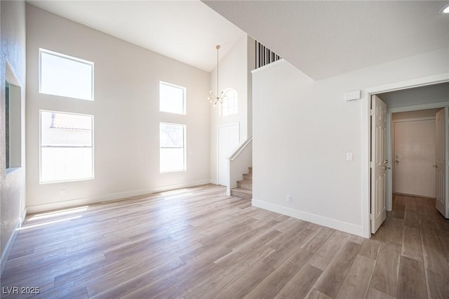 1620 Western Lily St, Las Vegas, NV 89128 - unfurnished living room featuring a towering ceiling, a chandelier, stairs, light wood-style floors, and baseboards