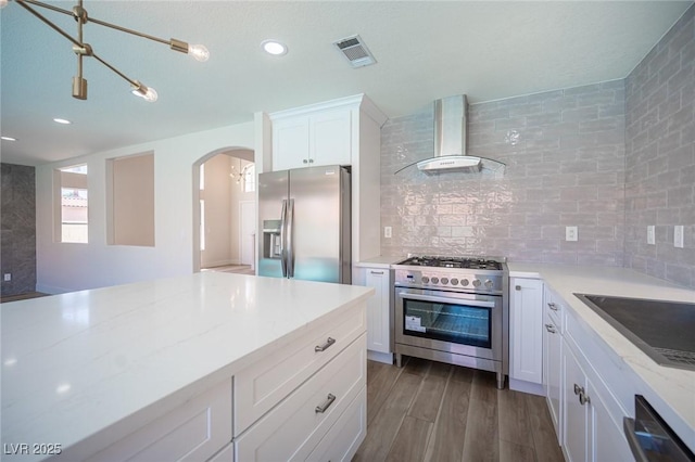 1620 Western Lily St, Las Vegas, NV 89128 - kitchen featuring appliances with stainless steel finishes, wall chimney exhaust hood, dark wood-style flooring, arched walkways, and white cabinetry