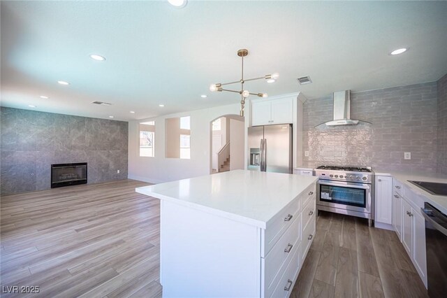 1620 Western Lily St, Las Vegas, NV 89128 - kitchen with stainless steel appliances, wall chimney exhaust hood, arched walkways, light wood-style flooring, and a kitchen island