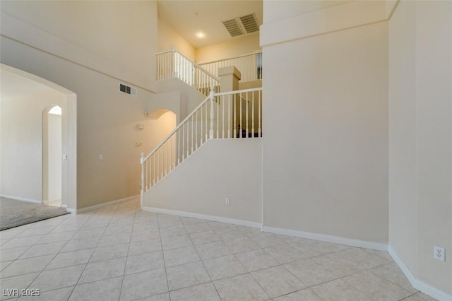 stairs with arched walkways, tile patterned flooring, baseboards, and a high ceiling