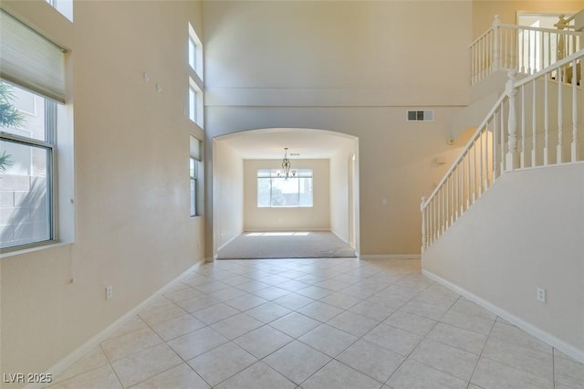 tiled entrance foyer featuring arched walkways, a high ceiling, stairway, baseboards, and a chandelier