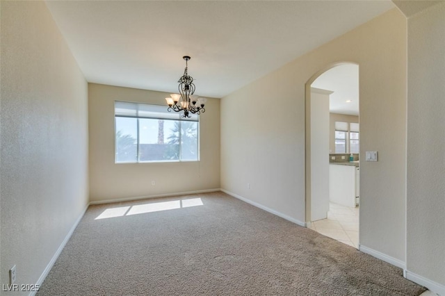 empty room featuring light colored carpet, arched walkways, a chandelier, and baseboards