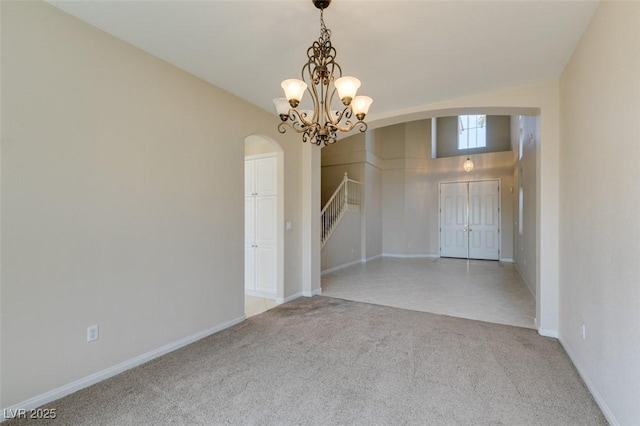 empty room featuring arched walkways, light colored carpet, stairs, a chandelier, and baseboards