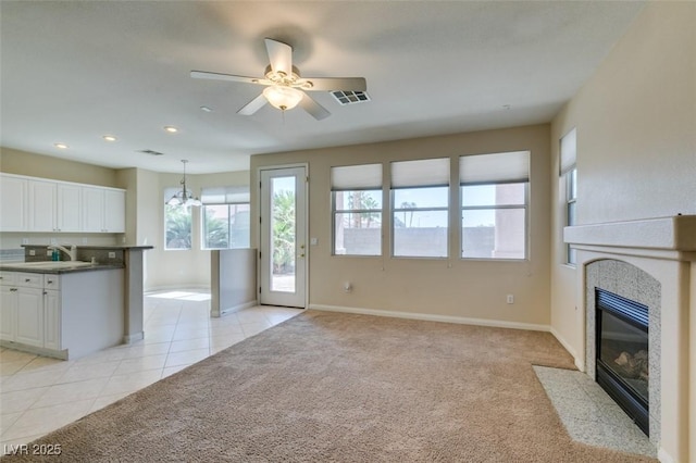 unfurnished living room featuring a fireplace with flush hearth, light tile patterned floors, baseboards, light carpet, and a ceiling fan