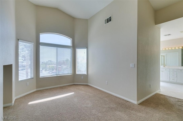 spare room with light colored carpet, a towering ceiling, and baseboards