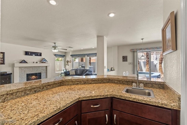 2024 Spruce Brook Dr, Henderson, NV 89074 - kitchen featuring a sink, a ceiling fan, open floor plan, light stone counters, and a glass covered fireplace