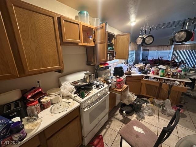 kitchen with white gas range oven, light tile patterned flooring, light countertops, and brown cabinets
