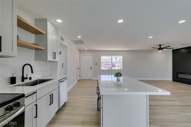 kitchen with a sink, appliances with stainless steel finishes, open shelves, baseboards, and light wood finished floors