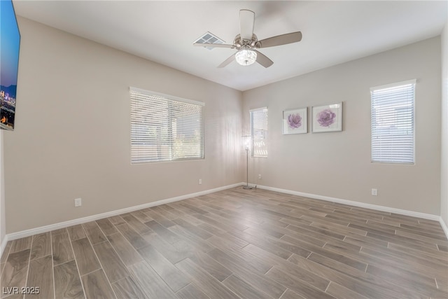 spare room with healthy amount of natural light, wood finished floors, a ceiling fan, and baseboards