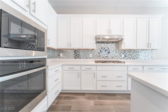 kitchen featuring appliances with stainless steel finishes, under cabinet range hood, white cabinetry, decorative backsplash, and light wood-style flooring