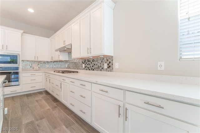 kitchen featuring appliances with stainless steel finishes, decorative backsplash, white cabinetry, under cabinet range hood, and recessed lighting