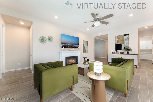 living room with a ceiling fan, a glass covered fireplace, wood tiled floors, recessed lighting, and baseboards