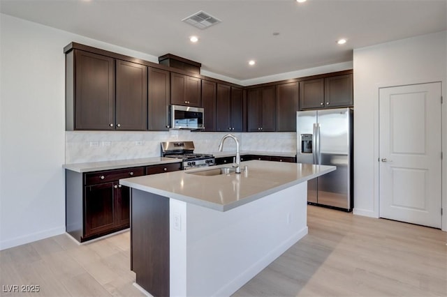 kitchen with stainless steel appliances, a sink, dark brown cabinetry, light wood finished floors, and recessed lighting