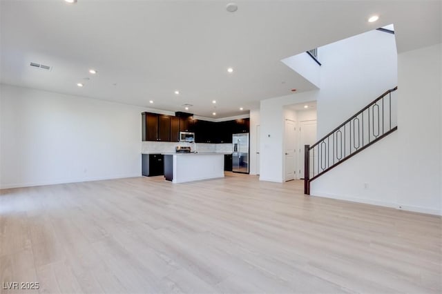 unfurnished living room with light wood-style flooring, baseboards, recessed lighting, and stairs