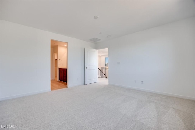 unfurnished bedroom with light colored carpet, ensuite bath, and baseboards