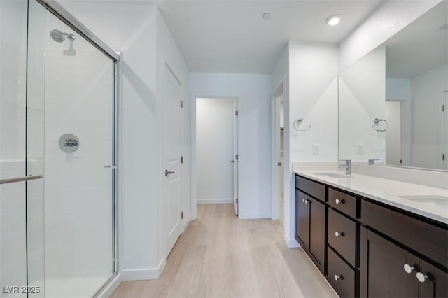 bathroom featuring a shower stall, wood finished floors, double vanity, and baseboards