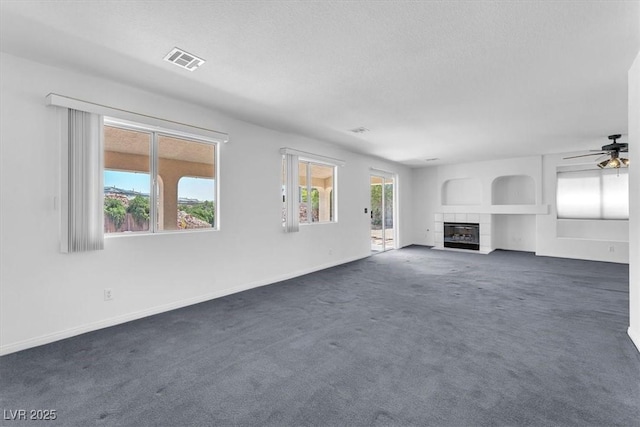 unfurnished living room with a fireplace, dark carpet, a ceiling fan, baseboards, and a textured ceiling